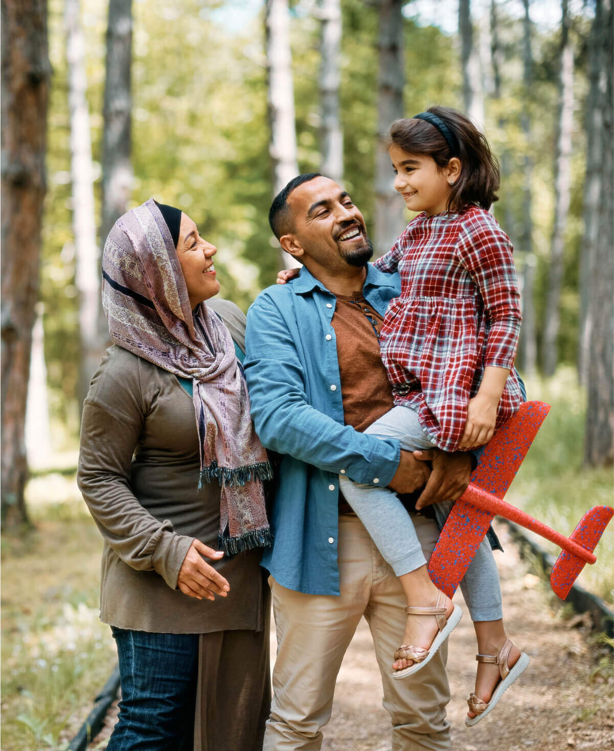 Father holding up daughter in arm with woman by side in a forest setting